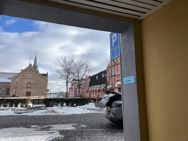 Udsigt fra porten i Møllergade mod gaden og havnen. På murpillen ved porten sidder et lille blåt skilt med teksten Indgang til Tin Tins Massage og en pil.